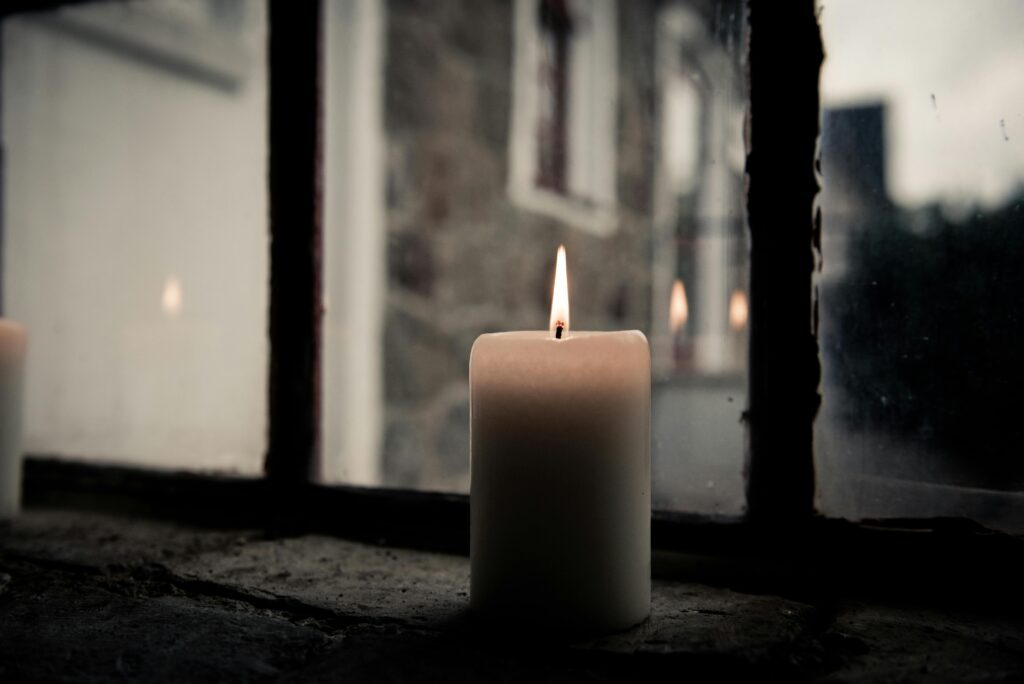 A lit candle by a window, offering a warm and cozy ambiance.