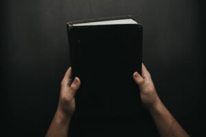 Hands holding a closed Bible against a dark background, symbolizing faith and spirituality.