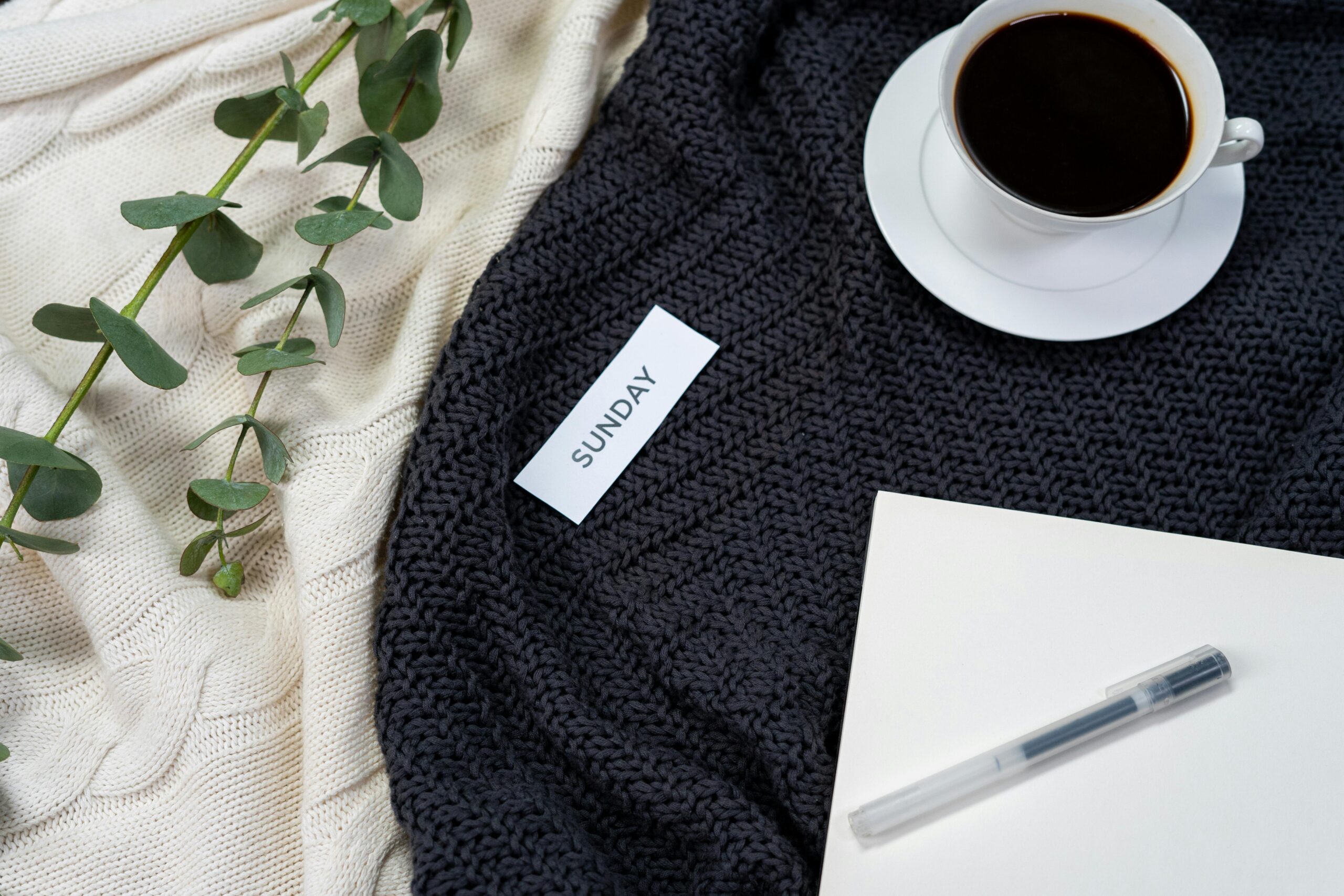 A flat lay of coffee, a knitted blanket, and a notepad creates a cozy Sunday atmosphere.