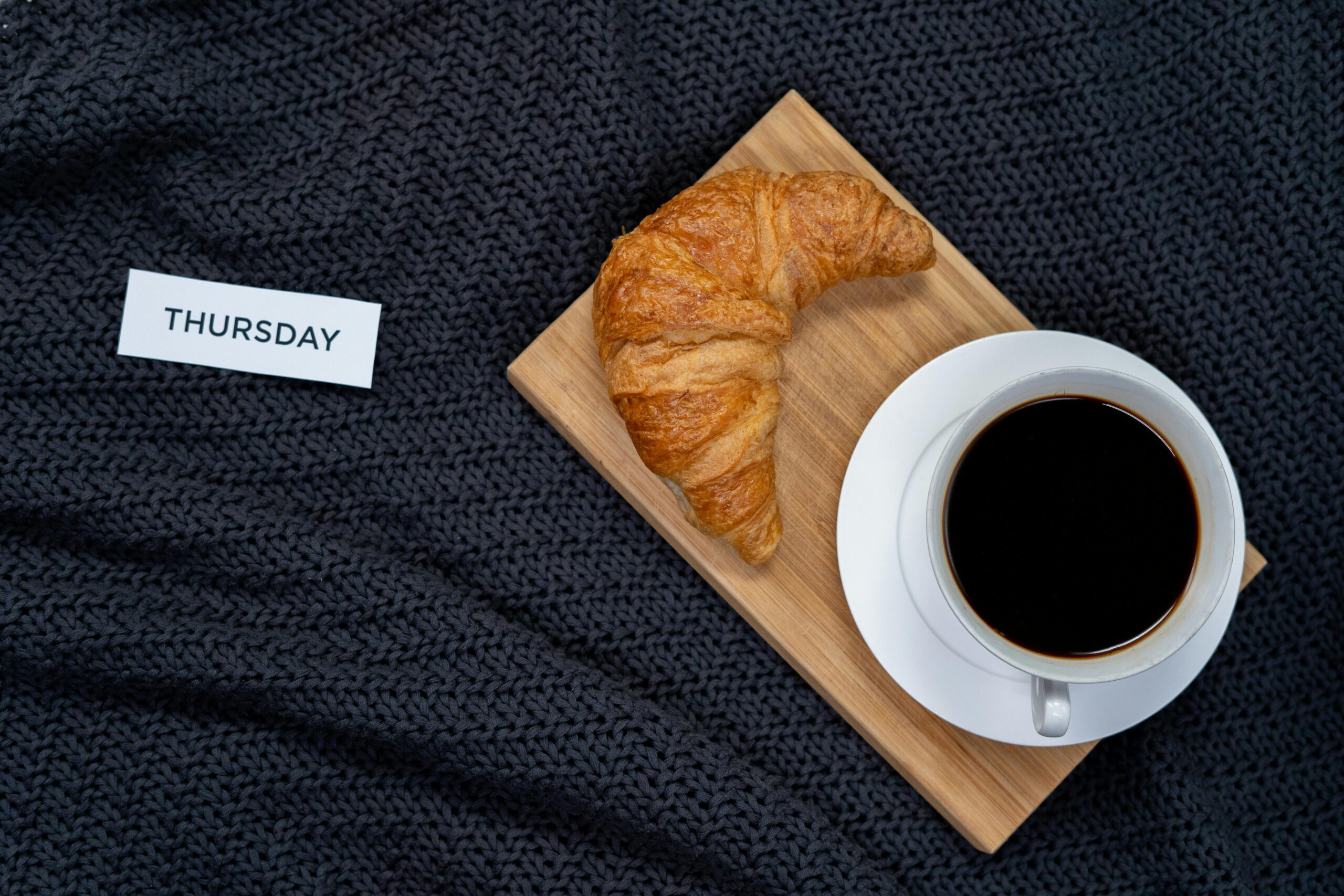 Enjoy a cozy Thursday morning with croissant and black coffee on a warm blanket.