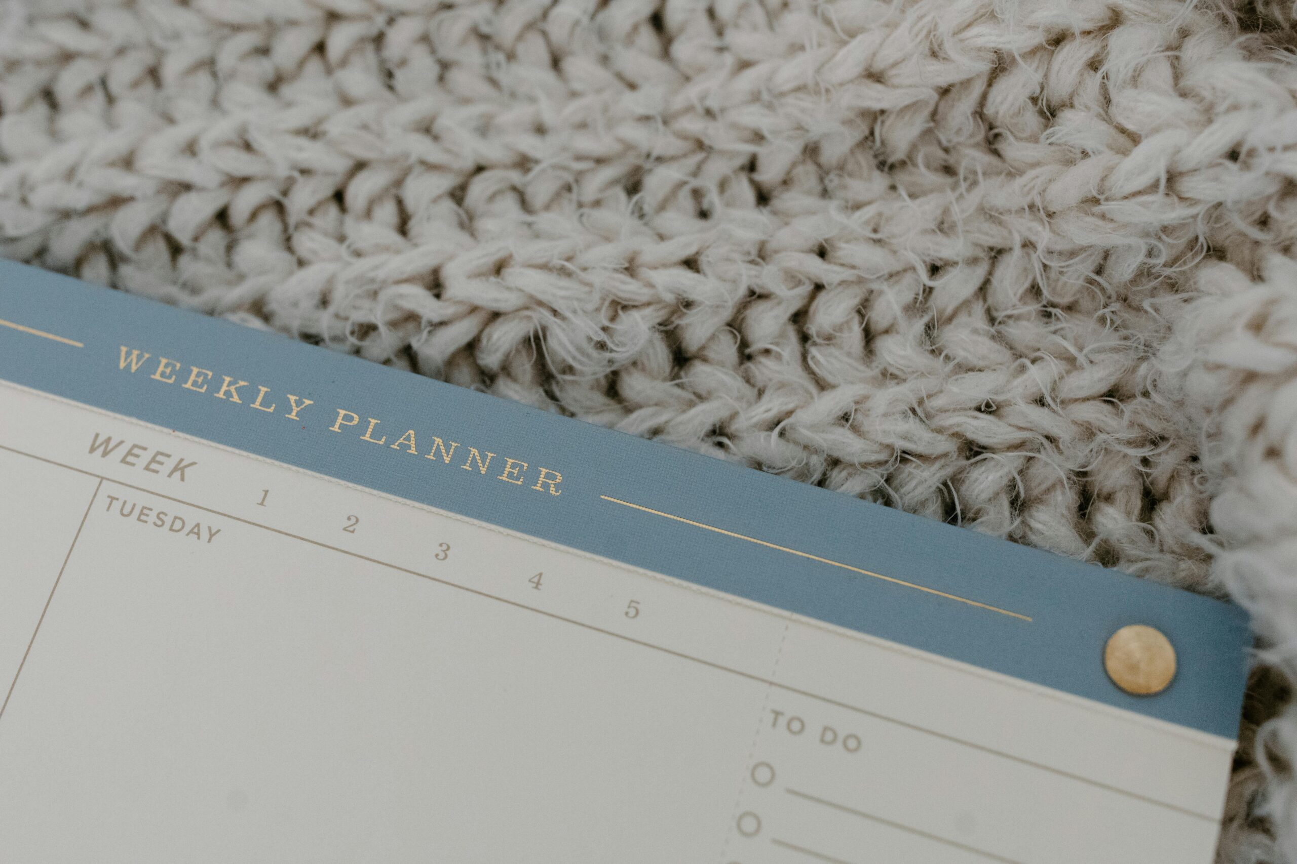 A weekly planner rests on a knitted fabric, providing a cozy vibe for planning.