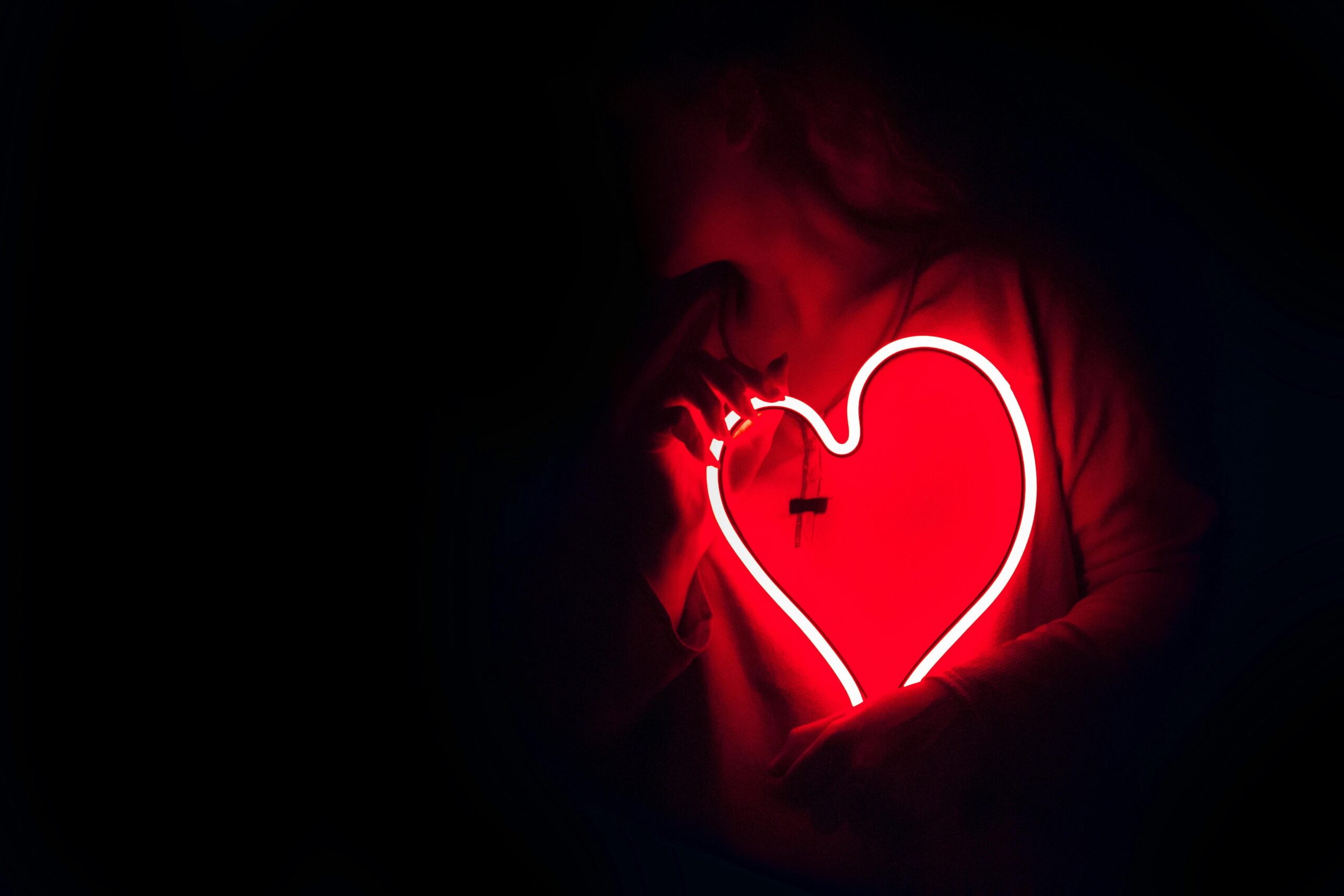 Silhouette of a person with a glowing red neon heart in the dark, symbolizing love.