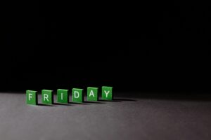 Green letter tiles spelling 'Friday' on a dark background, with dramatic lighting casting shadows.