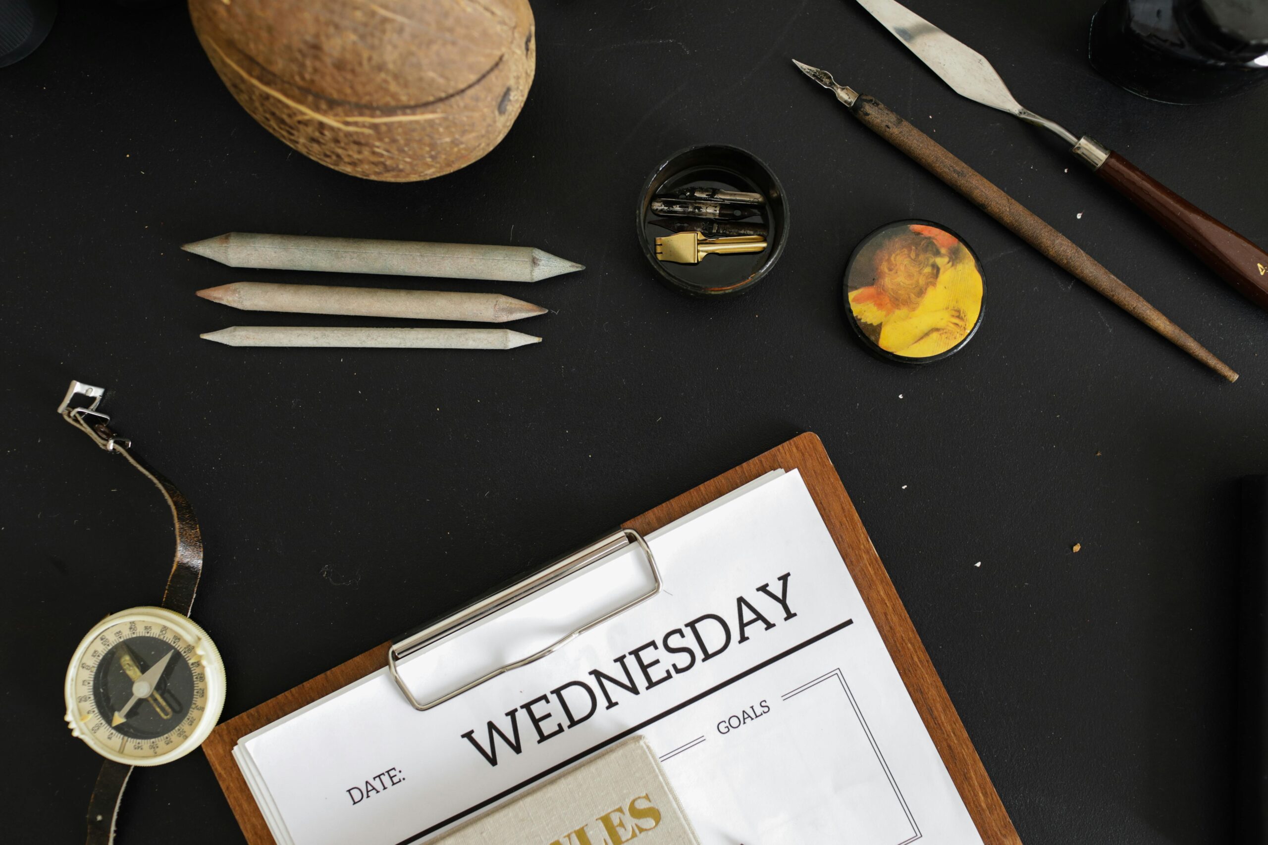 Overhead photo of a workspace featuring art supplies, a compass, and a Wednesday day planner.